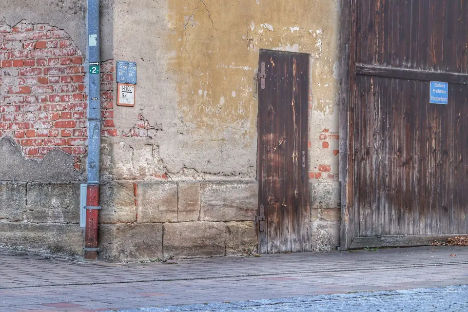 Verwitterte Stadtmauer mit abblätternder Farbe, alten Ziegelsteinen und einer Holztür, die auf Verfall hindeutet.